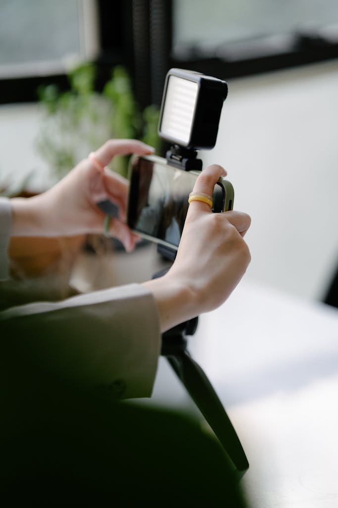 Close-up of hands operating smartphone on a tripod with LED light indoors.