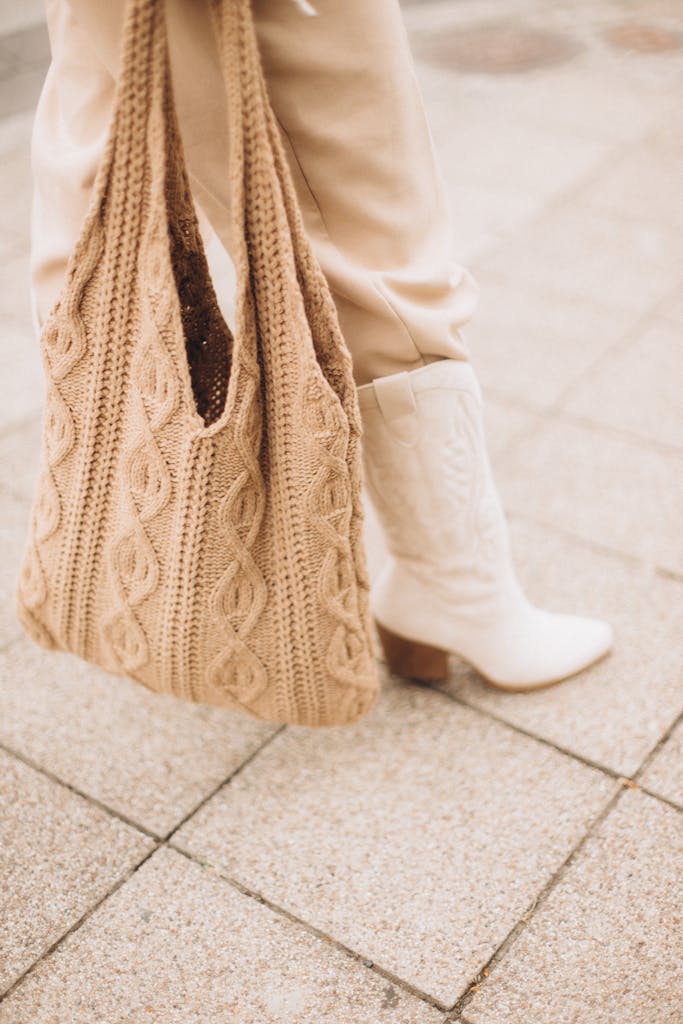 A beige knit bag and white boots showcased on outdoor pavement, offering an autumn fashion vibe.