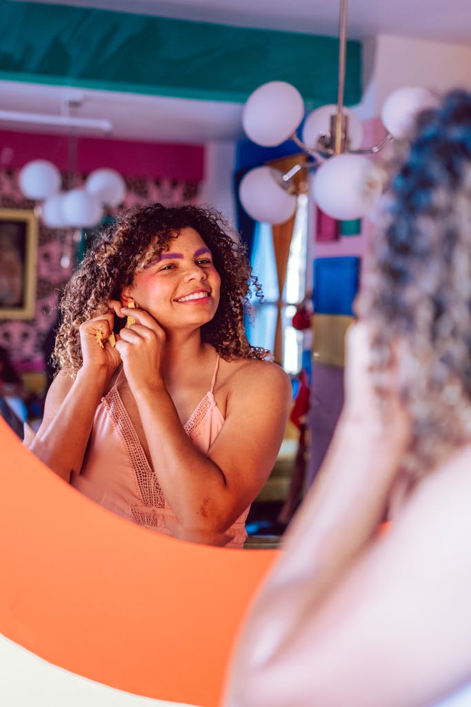 A young woman with curly hair smiling at her reflection in a colorful room.