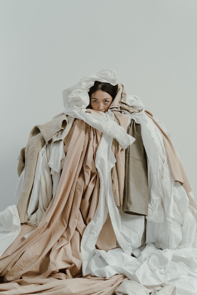 Asian woman partially hidden under layers of neutral-toned clothes.