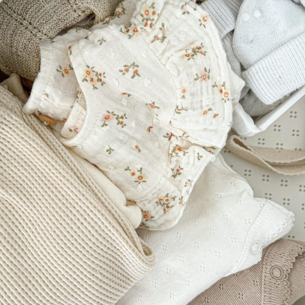 Minimalist flat lay of neutral-toned baby clothes with delicate embroidery.