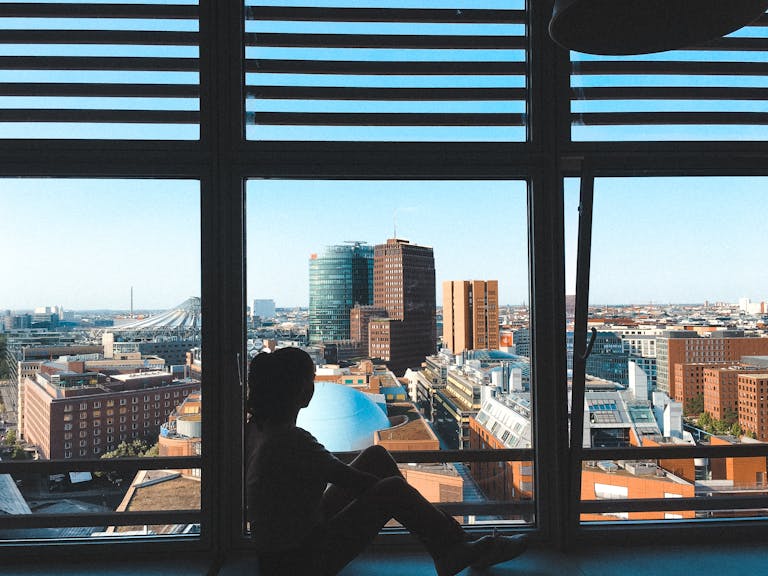 Silhouette of a person sitting by a window overlooking the Berlin cityscape.
