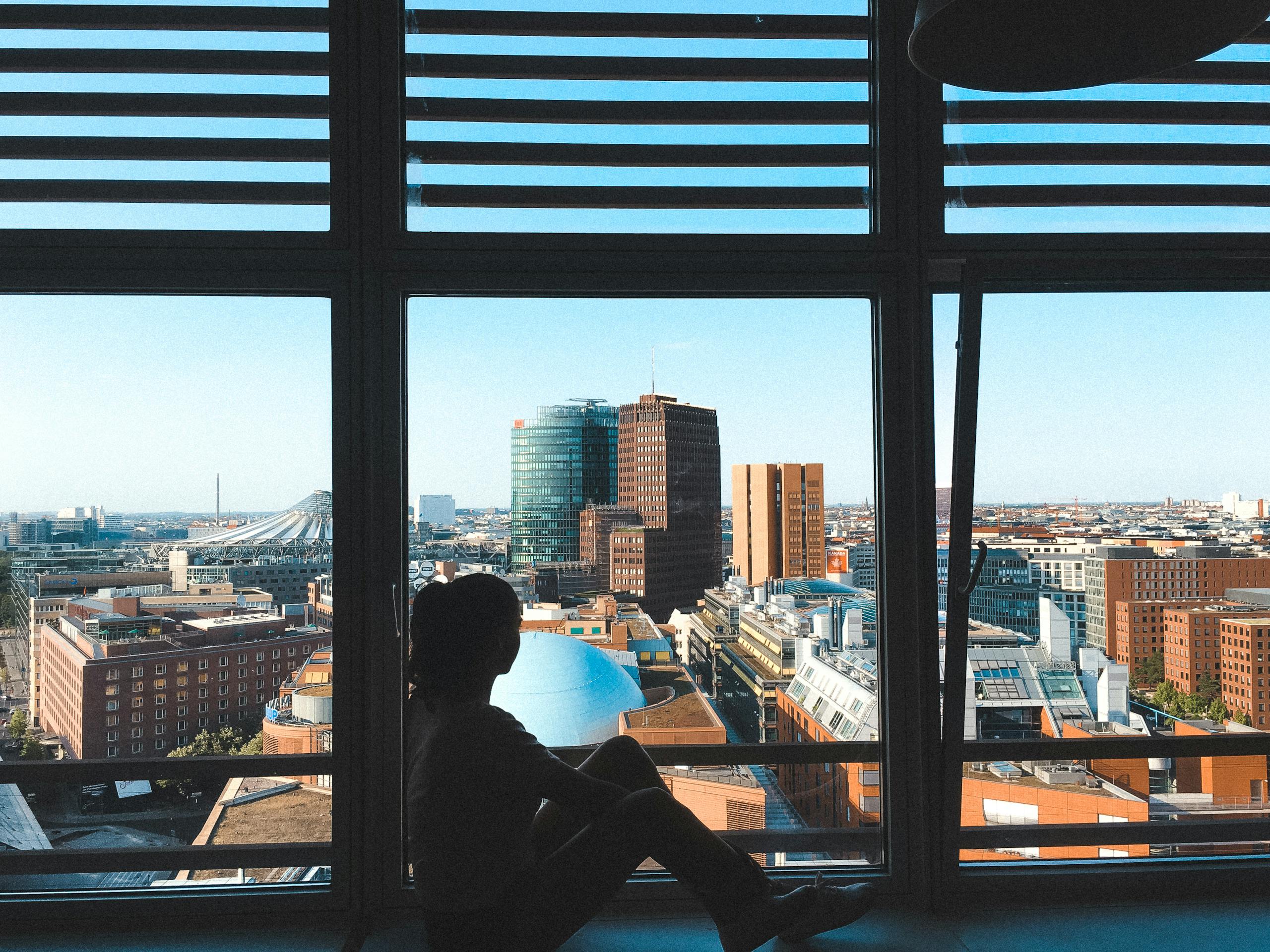 Silhouette of a person sitting by a window overlooking the Berlin cityscape.