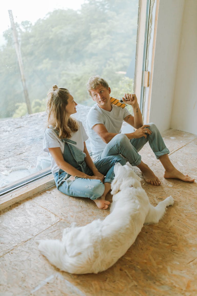 Young couple sitting indoors with a dog, enjoying a break during home renovation.
