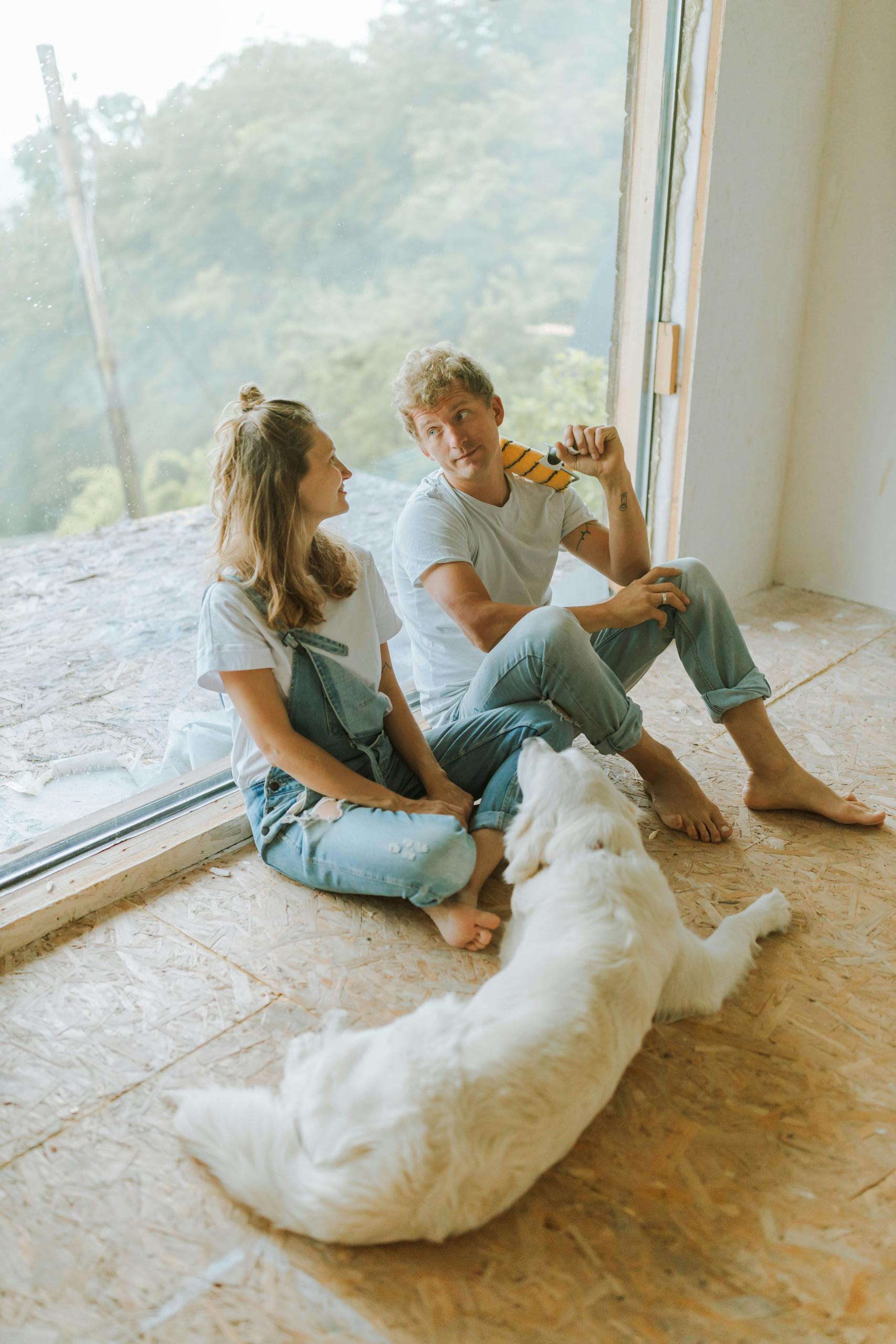 Young couple sitting indoors with a dog, enjoying a break during home renovation.