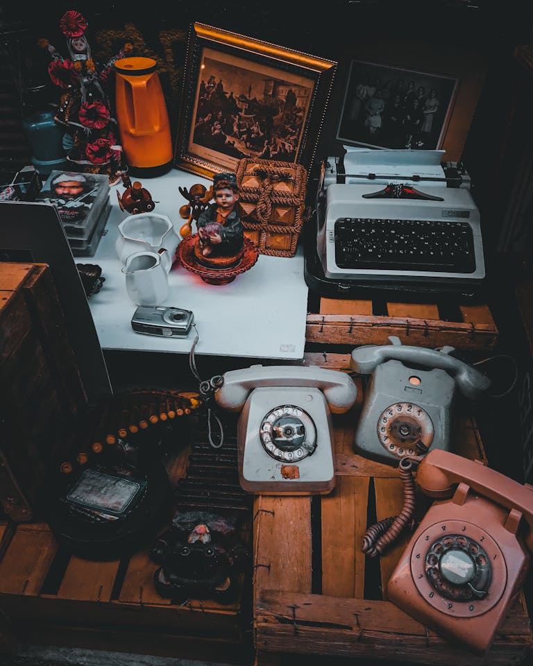 A collection of vintage items including rotary phones, typewriter, and figurines in a rustic setting.