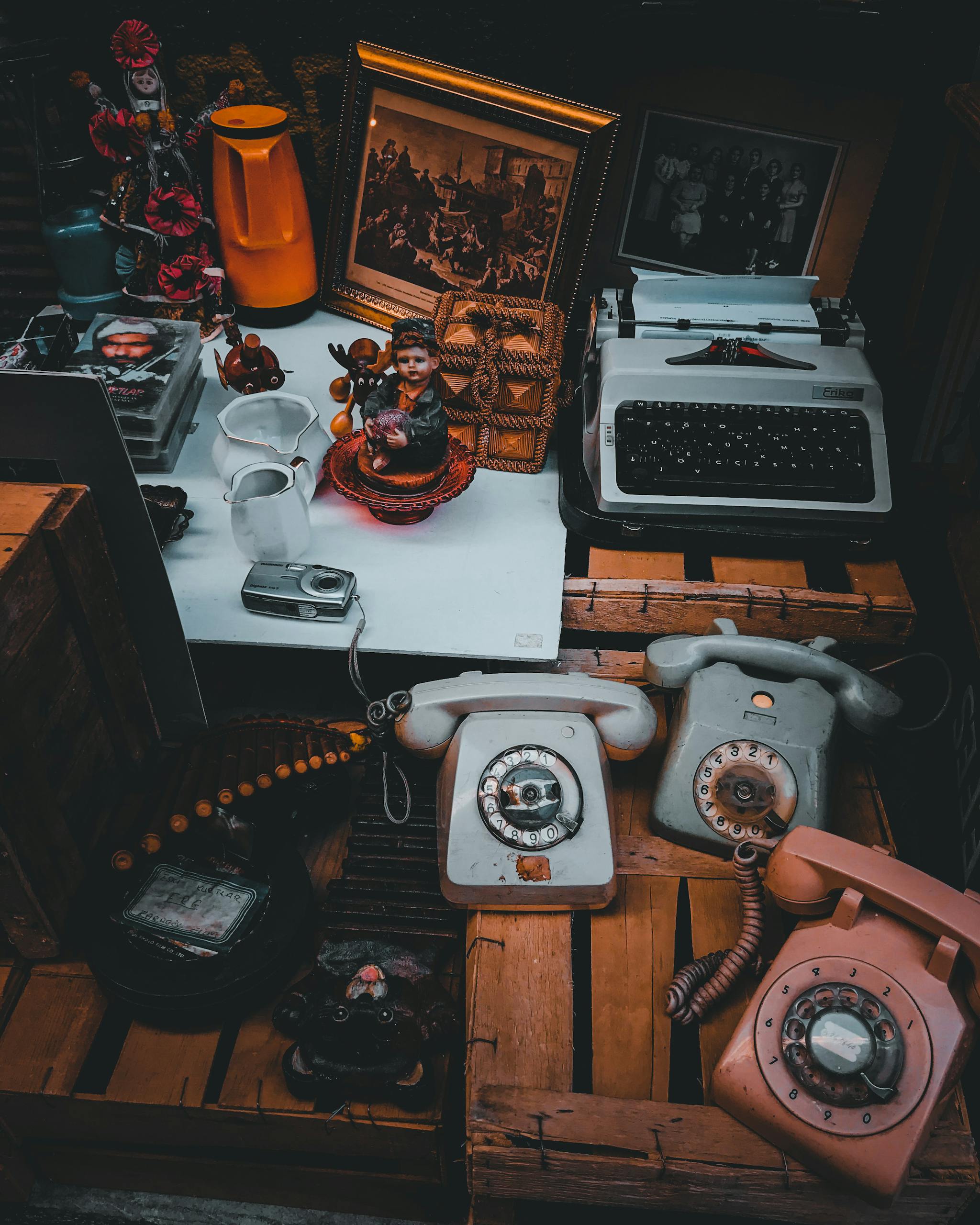A collection of vintage items including rotary phones, typewriter, and figurines in a rustic setting.