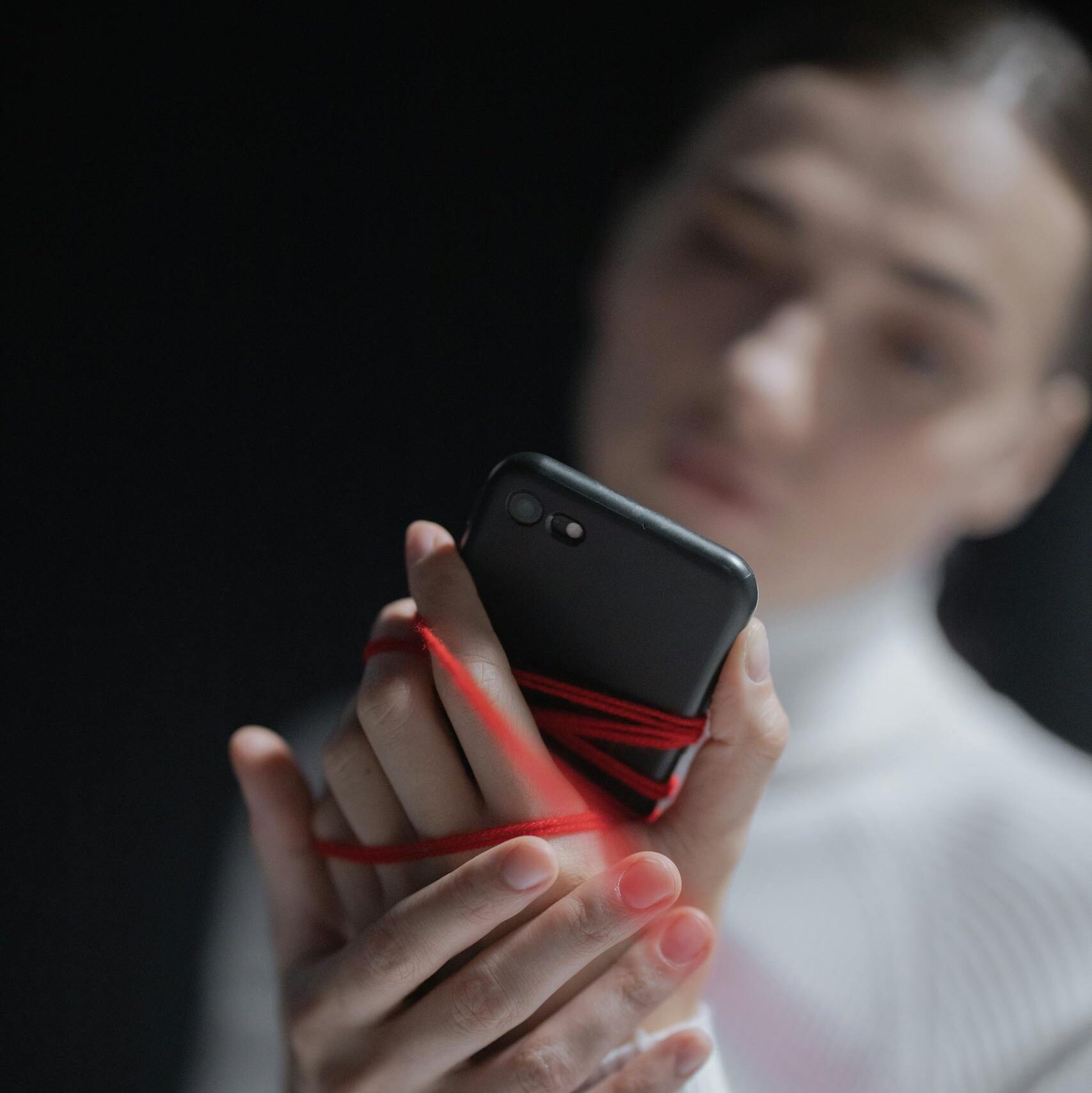 A woman tied with red thread holds a smartphone, symbolizing tech addiction.